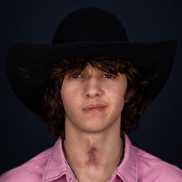 Teenage boy in pink shirt and black cowboy hat.