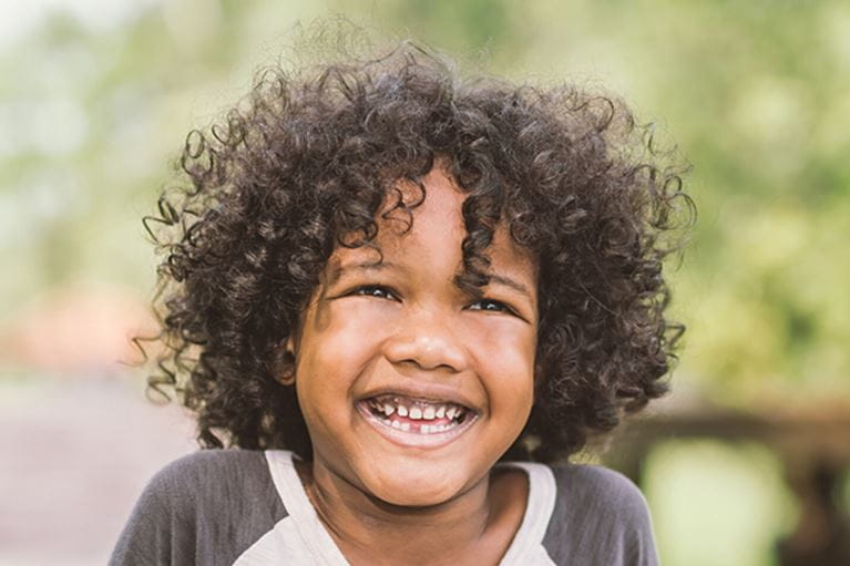 Boy with curly hair grinning at camera.