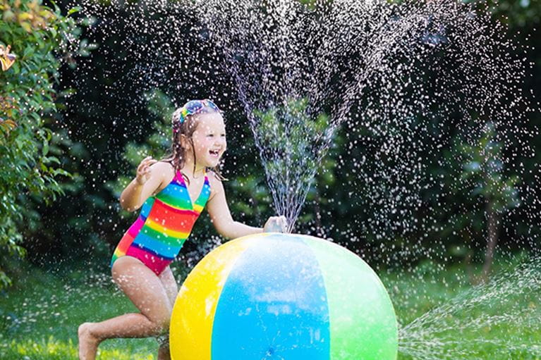 Small girl in bathing suit playing with a water ball.