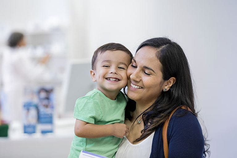 Mom in white shirt holding toddler son in green shirt.