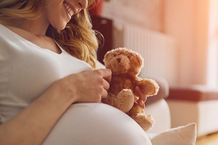 Mom holding small teddy bear near pregnant belly.