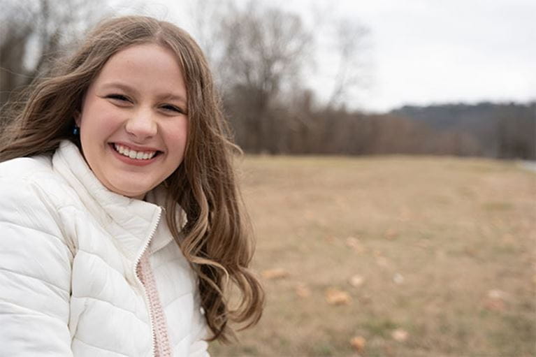 Smiling teenage girl outside wearing white winter coat.