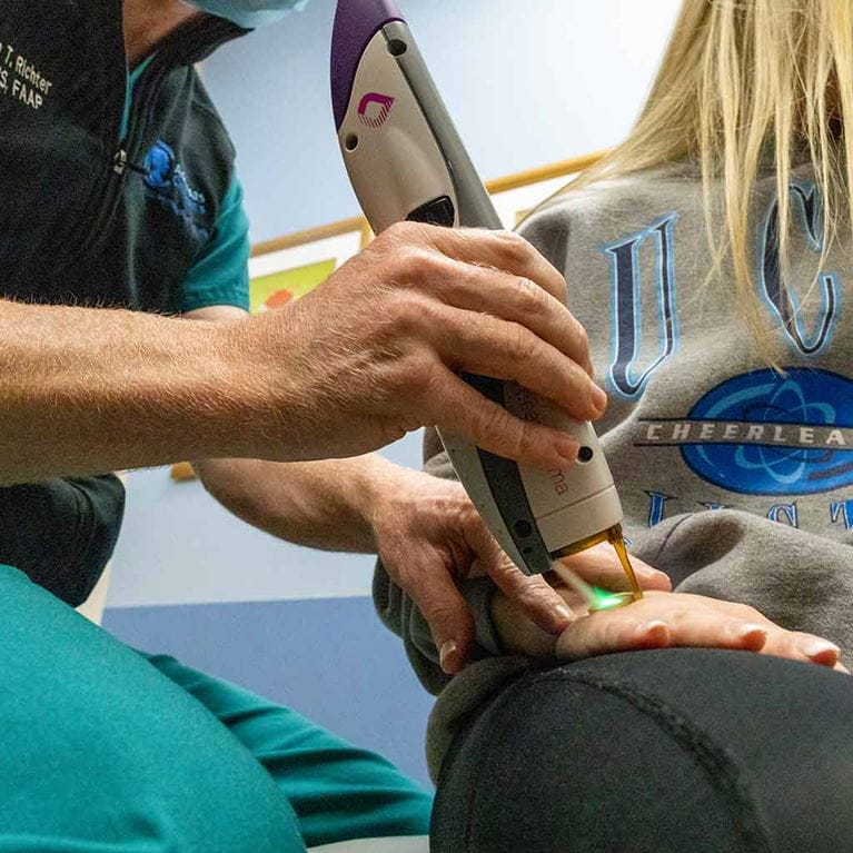 Teenage girl receiving laser treatment on hand.