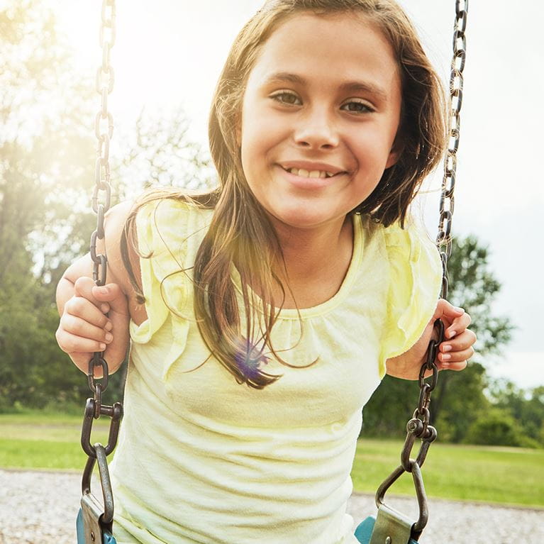 Girl in yellow shirt swinging in the park.
