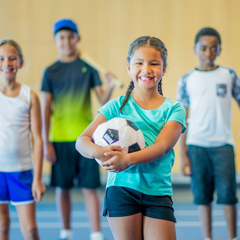 Kids standing in gym with soccer ball in hand.