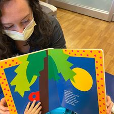 Child Life Specialist wearing mask and showing book to patient.