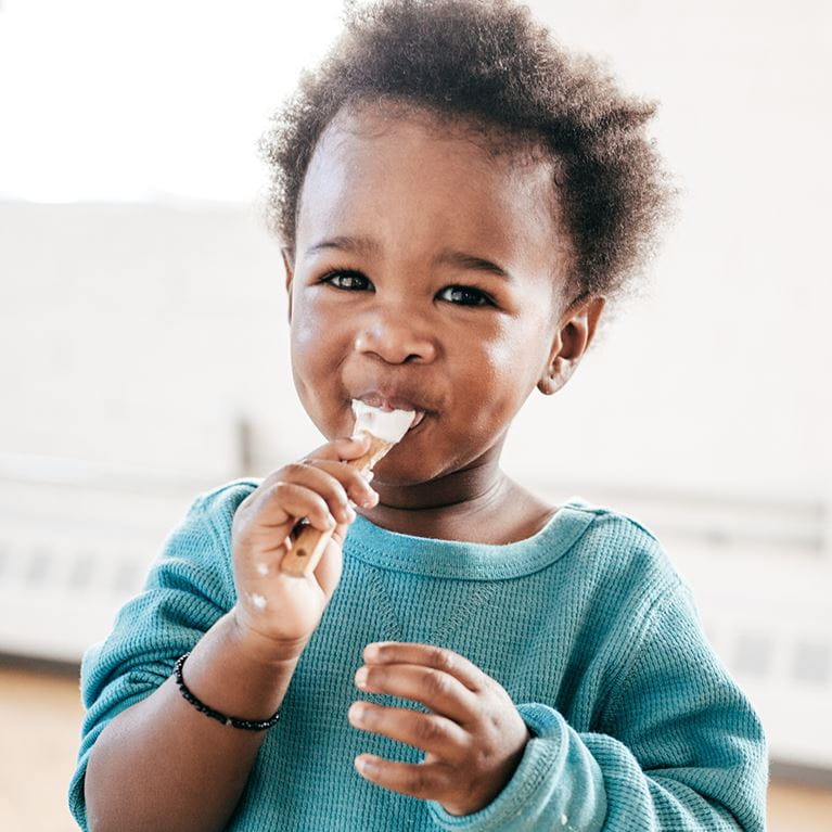 Young boy licking a spoon and smiling.