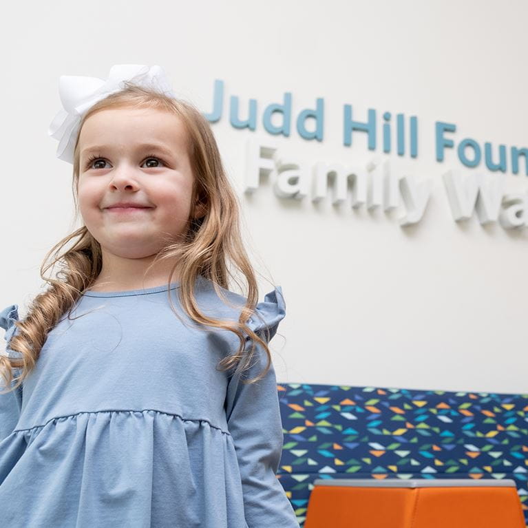 Girl with blue dress and white hairbow standing in waiting room.