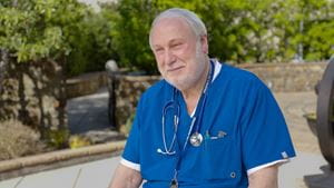 Male employee in blue scrubs sitting outside.