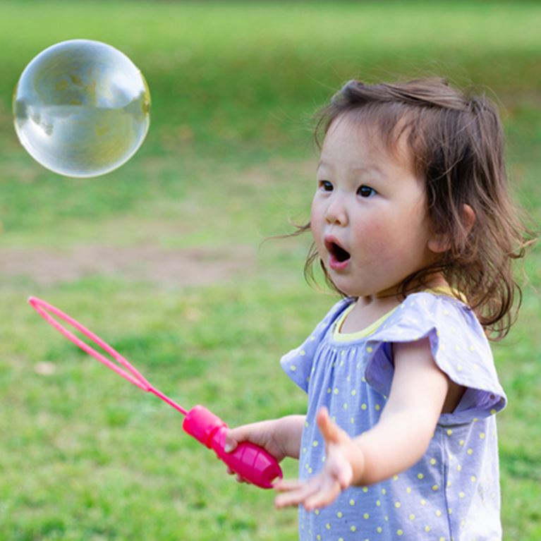 Young girl outside playing with bubbles.