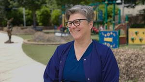 Female employee in blue scrubs sitting outside.