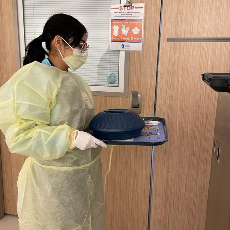 Food host with food tray at patient door in yellow protective wear.