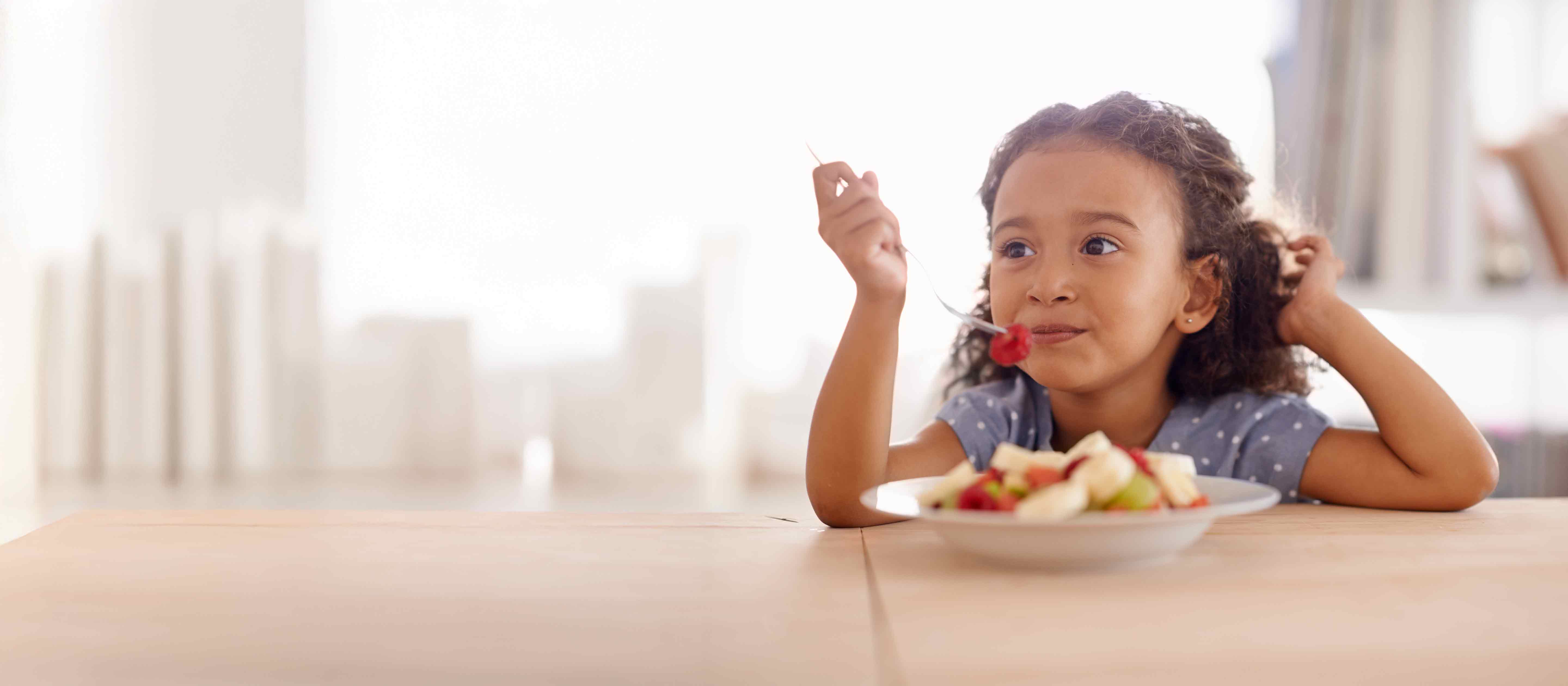 Little girl eating bowl of fruit.