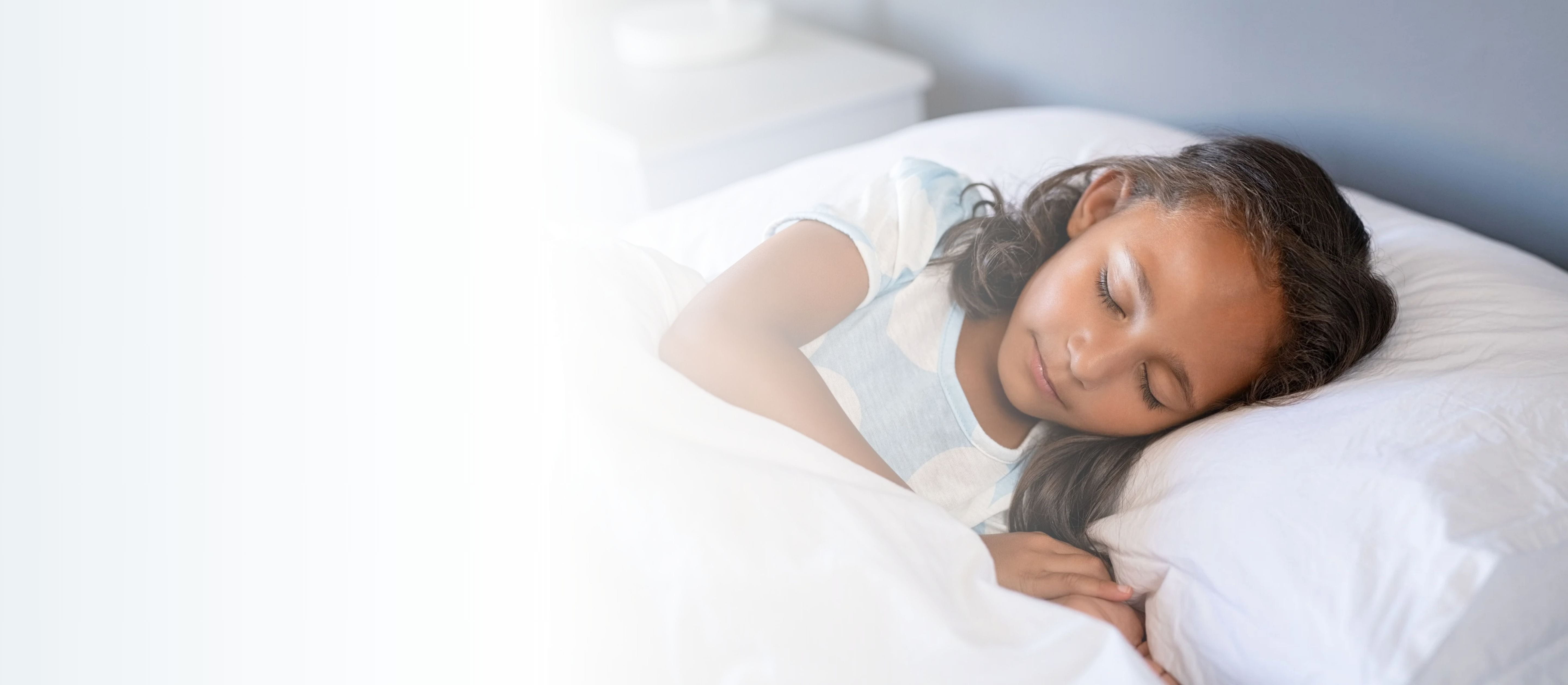 Close up face of female child with eyes closed sleeping under white blanket.
