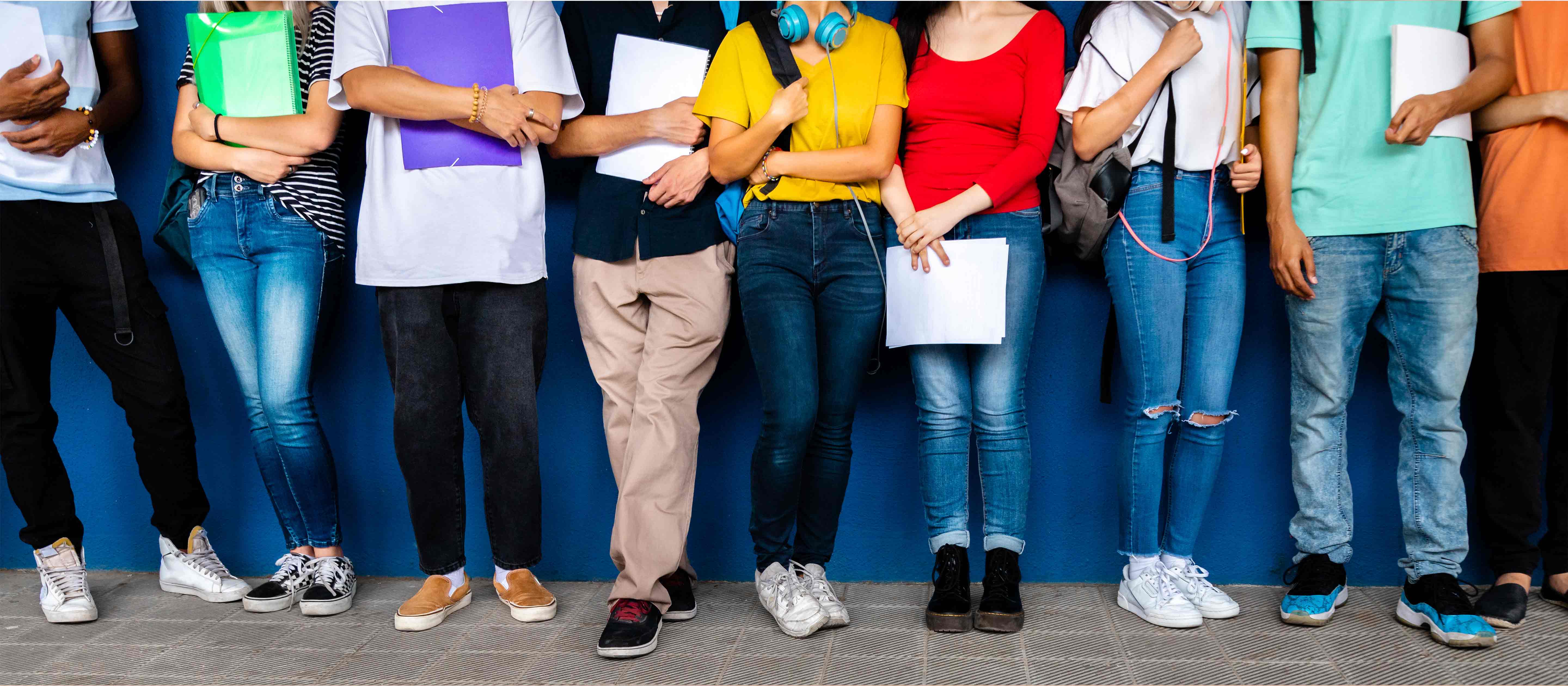 Image of group of teenage high school students ready to go back to school standing against blue background wall.