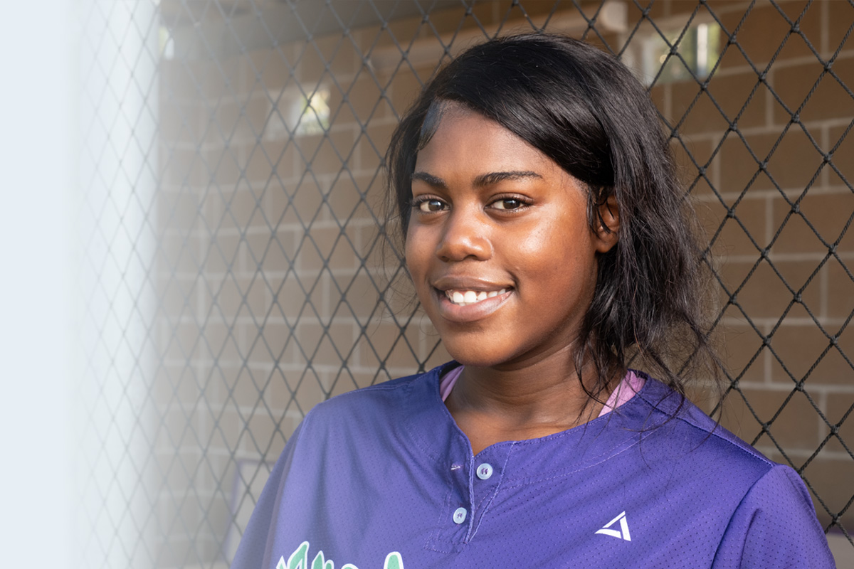 Softball player wearing purple jersey. 