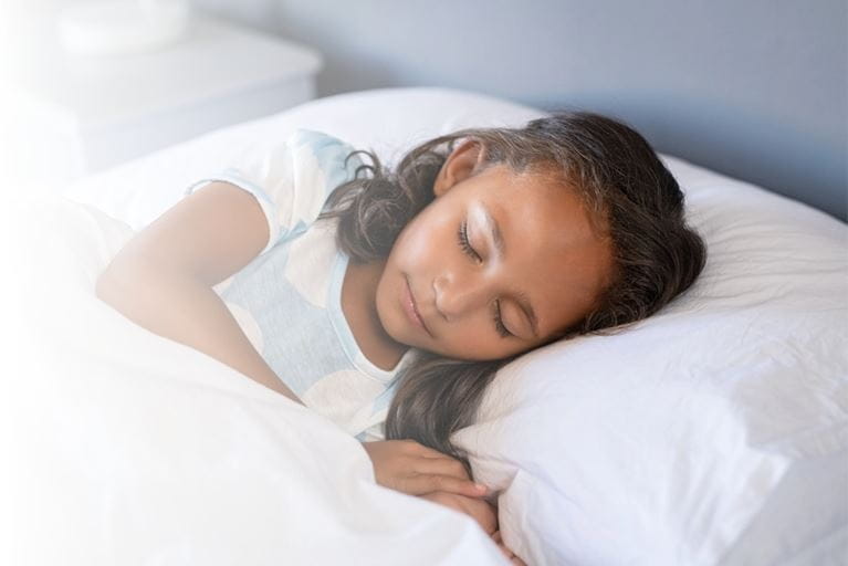 Close up face of female child with eyes closed sleeping under white blanket.