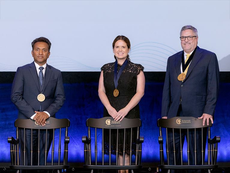 Photo of three investiture honorees, each standing behind endowed chairs.