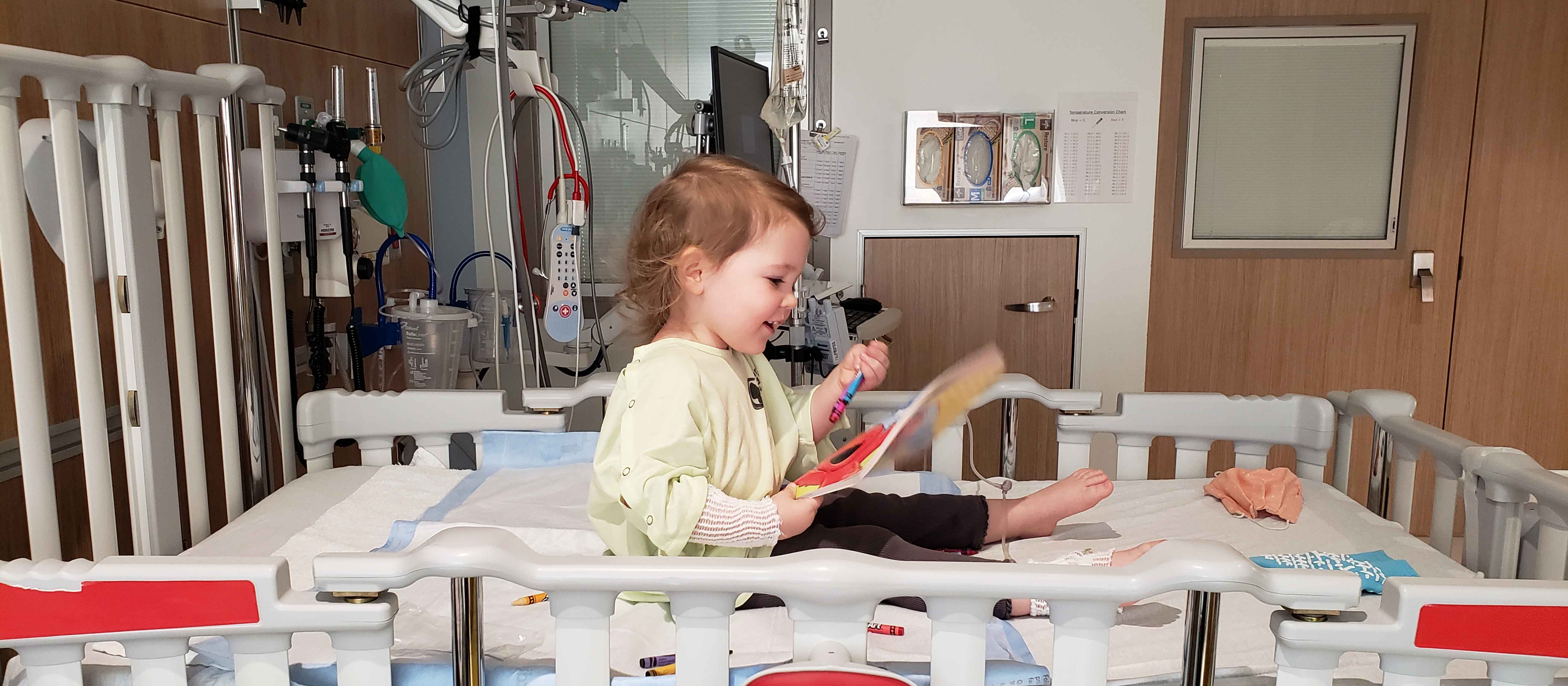 Small toddler playing with toys in hospital bed.