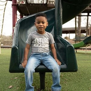 Happy African-American boy sitting on a slide in the park.