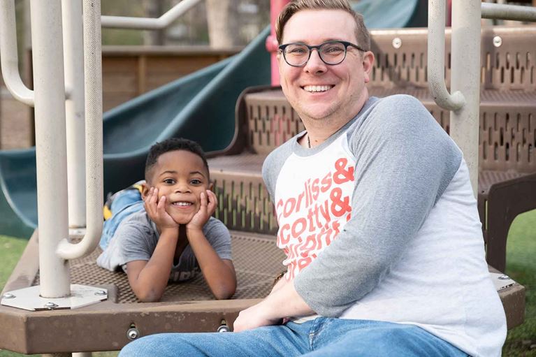 Father and son sitting on gym set in the park, smiling. 