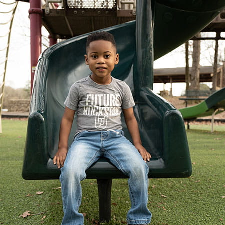 Happy African-American boy sitting on a slide in the park.