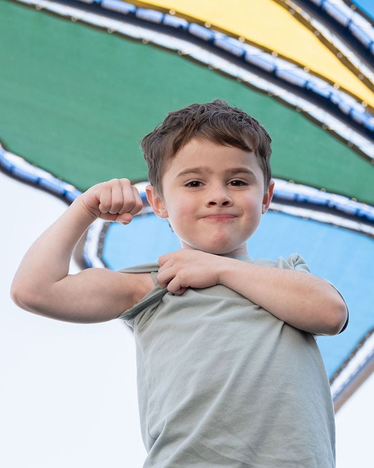 Boy in green shirt and brown shorts plays on playground outside ACH.
