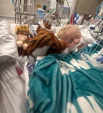 Photo of Landon, a happy little boy sitting in red wagon with balloons.