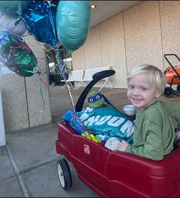 Photo of Landon, a happy little boy sitting in red wagon with balloons.